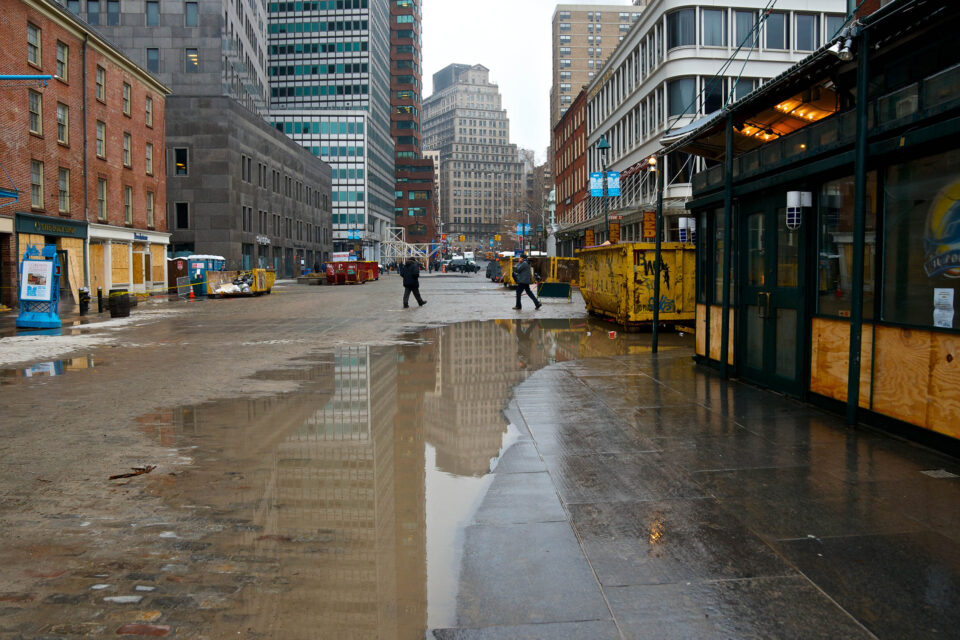 New York City, USA - December 10, 2012: Two men seen passing by Front and Fulton Streets at the South Street Seaport-Fulton Market district in Lower Manhattan. Six weeks after Hurricane Sandy's flood water severely damaged the area retail shops are boarded up and dumpsters are being filled with flood damaged debris.