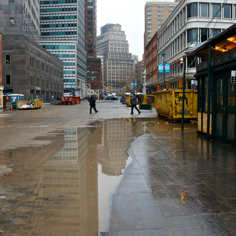 New York City, USA - December 10, 2012: Two men seen passing by Front and Fulton Streets at the South Street Seaport-Fulton Market district in Lower Manhattan. Six weeks after Hurricane Sandy's flood water severely damaged the area retail shops are boarded up and dumpsters are being filled with flood damaged debris.