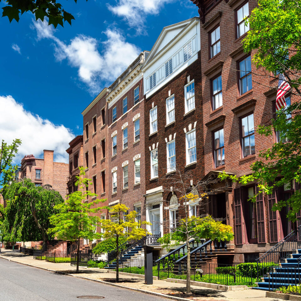 A scenic street lined with historic brick rowhouses and green trees under a bright blue sky on a sunny summer day in Albany, New York, United States