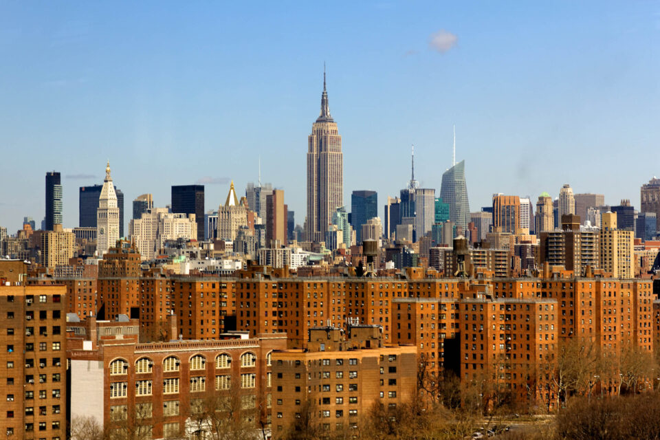 The New York City midtown Manhattan skyline with the landmark Empire State Building in the center and contrasting drab brown apartment blocks in the foreground. Shot from across the East River in early spring.