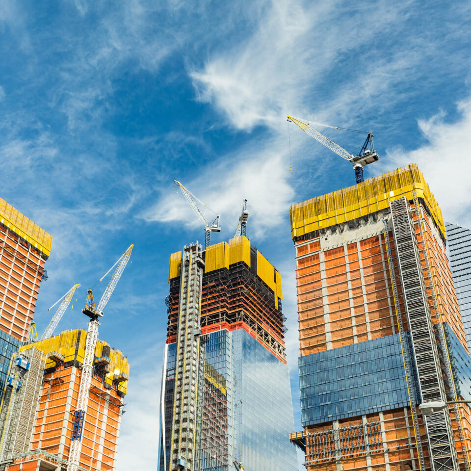 Skyscrapers construction site for modern buildings in New York. Cranes and scaffolding used to build tall structures, blue sky on background.